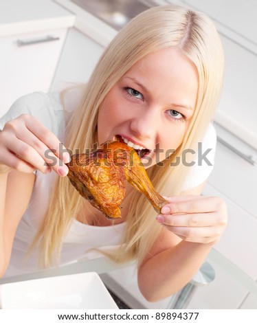 beautiful young blond woman eating chicken in the kitchen at home