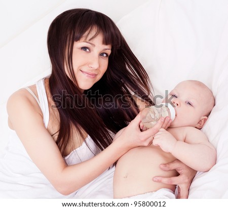 happy young mother and her one year old daughter drinking water in bed at home