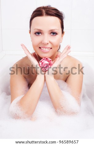 beautiful young brunette woman taking a relaxing bath with foam and holding a flower-shaped soap
