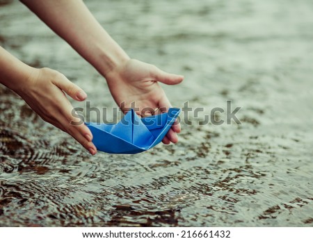 hands of a young woman with a paper boat by the lake in summertime (focus on the beat)