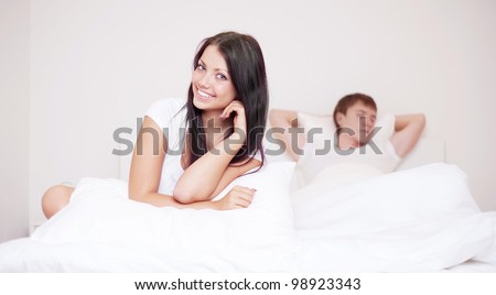 happy young woman and  sleeping man in bed at home (focus on the woman)