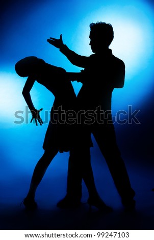 A silhouette of a couple dancing, against blue studio background