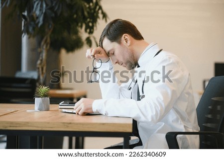 Stressed male doctor sat at his desk. Mid adult male doctor working long hours. Overworked doctor in his office. Not even doctors are exempt from burnout Stok fotoğraf © 