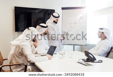 Cinematic image of an arabian group of people working in the office. Four men wearing traditional outfit from Dubai making business plans indoor