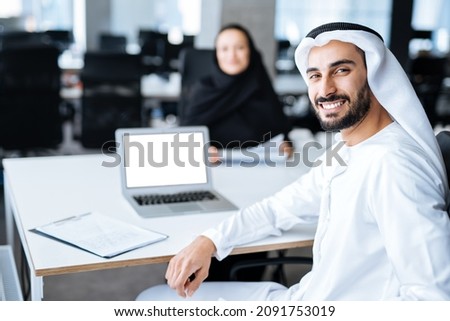 Man and woman with traditional clothes working in a business office of Dubai. Portraits of  successful entrepreneurs businessman and businesswoman in formal emirates outfits. Concept about middle east Imagine de stoc © 