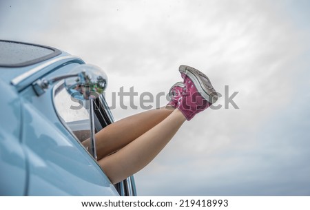 woman lying down in her car. legs out. concept of freedom and carefree. Car and shoes give a vintage touch to the image
