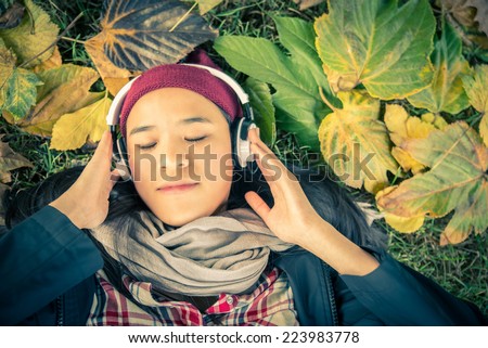 Young asian girl listening music in park. Student girl outside listening music with headphones and autumn leaves in the background