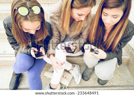 Girls typing on mobile phones - Three friends holding smart phones and chatting - Students sitting outdoors on stairs and talking