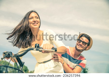 Happy couple riding bikes in the city - Young pretty woman driving bicycle and playful man sitting behind - Portrait of two lovers outdoors