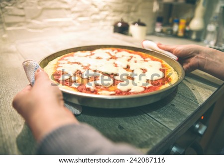 Woman taking out handmade pizza margherita from oven - Candid image of italian pizza preparation