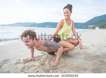 playful couple on the beach. boyfriend making push ups, and girlfriend sitting on his back