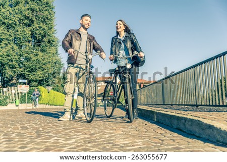 Couple riding on bicycles  and having fun - Tourists driving around the city - Two friends walking with bikes on the streets