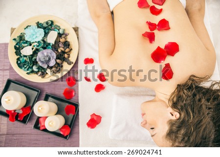 Spa treatment - Beautiful young woman lying on a massage bed with roses and candles and relaxing after a working day - Woman having massage in elegant and relaxing atmosphere