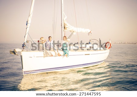 Group of young people sitting on a sailing boat - Two beautiful women and attractive man having fun on a boat while on vacation - Rich people enjoying party