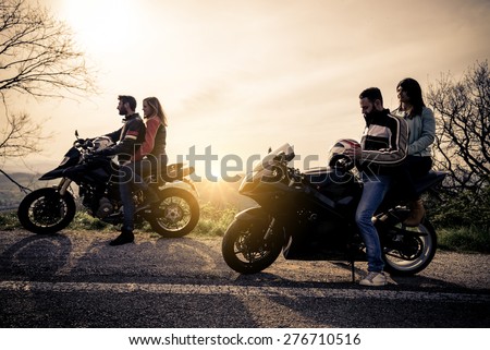 Two motorbikes driving in the nature - Friends driving racing motorcycles with their girlfriends - Group of bikers stop in a panoramic view point and look at suggestive sunset