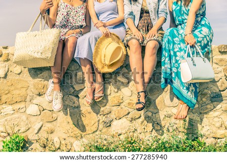 Four girlfriends sitting on a wall outdoors with spring and summer dresswear - Women meeting and having fun in a countryside - Concepts about friendship,seasonal,lifestyle and shopping