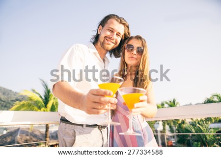Attractive couple at party talking and having fun in a cocktail bar - Two young persons drinking aperitif at sunset in a luxurious hotel