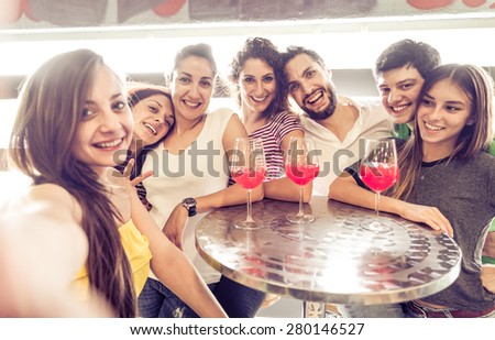 Group of friends taking selfie with smartphone in a lounge bar - People celebrating in a club, looking at camera and having some cocktails