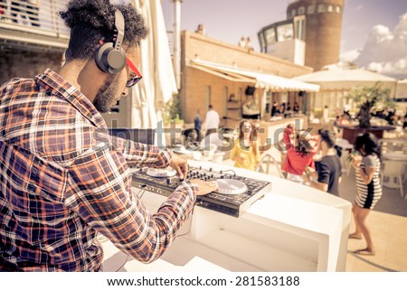 Dj playing trendy music in a open air club - People dancing and partying while the disc jockey mixes two song tracks in the console at a summer concert