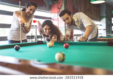 group of friends playing pool. the girl is focusing on the next shot. concept about leisure, fun, friendship and people