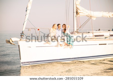 Group of young people sitting on a sailing boat and taking a selfie - Two beautiful women and attractive man having fun on a boat while on vacation