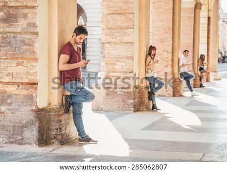 Young people looking down at cellular phone - Teenagers leaning on a wall and texting with their smartphones - Concepts about technology and global communication