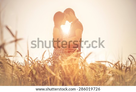 young couple kissing in a field. asian woman hugging a caucasian man in the middle of a wheat field and kissing each other. concept about passion and love