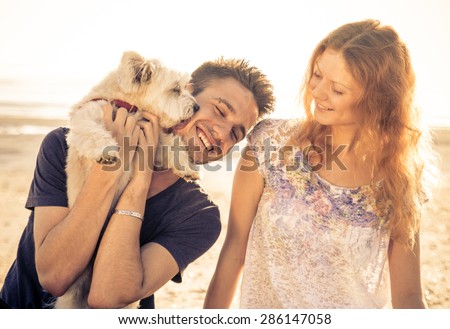 couple walking with dog outdoor. man holding up the cute dog while he licks his face