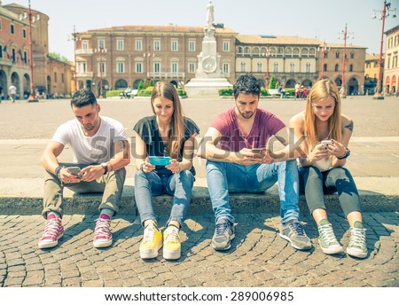 Young people looking down at cellular phone - Teenagers sitting outdoors and texting with their smartphones - Concepts about technology and global communication
