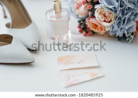 Wedding accessory bride. Stylish beige shoes, earrings, gold rings, flowers, garter, perfumes on table standing on wooden background. Letters from the bride and groom. flat lay. top view. Сток-фото © 