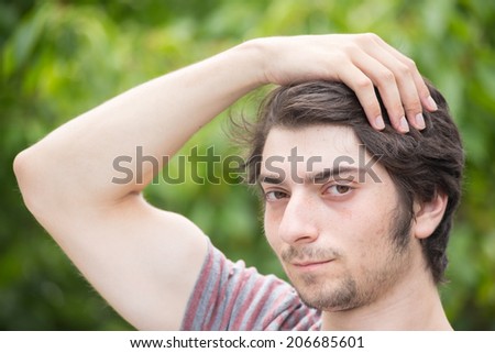 A young male model is brushing through his hair attractively and looking into the camera