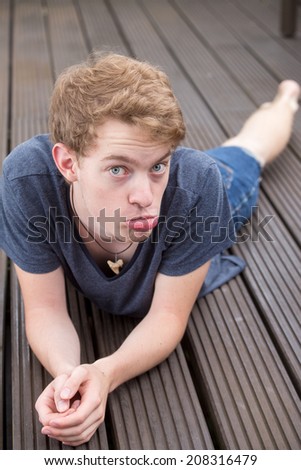 A young blonde male model is pouting on a dark wooden background