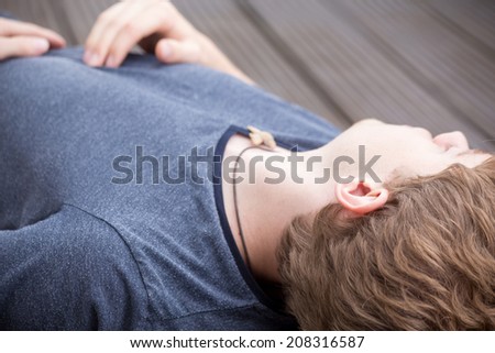 A young blonde male model is sleeping peacefully on a dark wooden background closeup