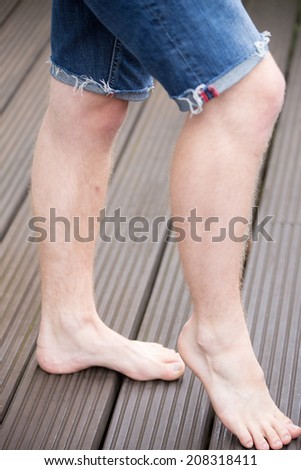 Beautiful feet from a young male model are walking on dark wooden planks - side view