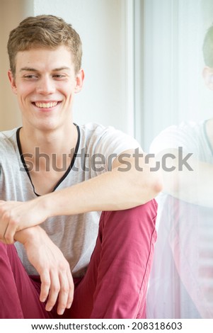 A young male model is smiling to the left with his arms resting on his legs, portrait