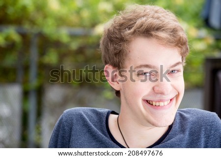 A young blonde male model is smiling into the camera with a wide grin on his face with a nice modern background