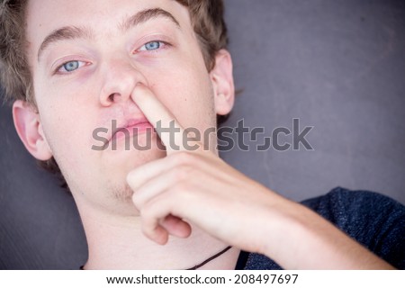 A young blonde male model is picking his nose with a nice modern grey background