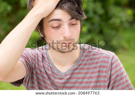A young male model is brushing through his hair and looking down, the right - lifting his eyebrows in surprise
