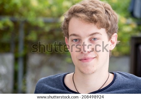 A young blonde male model is smiling into the camera and has a smirk on his face with a nice modern background
