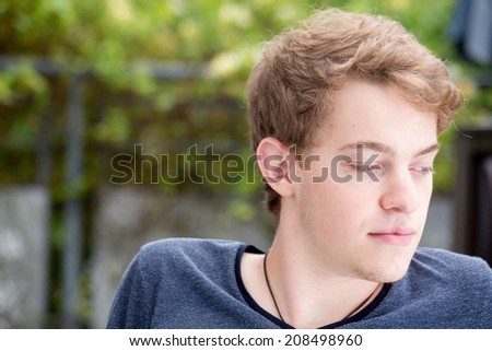 A young blonde male model is looking down and thinking/worrying