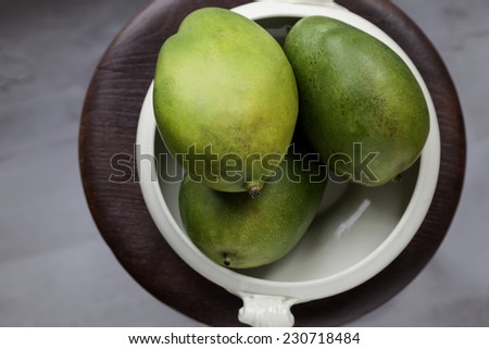 Three ripe mangoes in the white ceramic bowl viewed from above