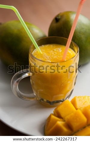 The glass of fresh mango smoothie with ripe mangoes on the white plate