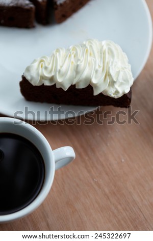 Slice of Belgium chocolate cake with whipped cream on the top with a cup of black coffee