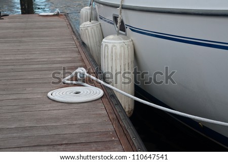 Boat secured to a wooden dock or pier.  Shows side of boat and rubber fenders along side the dock.