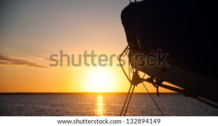 Sun setting over the ocean with the boom and mainsail of a sailboat in the foreground.  copy space available