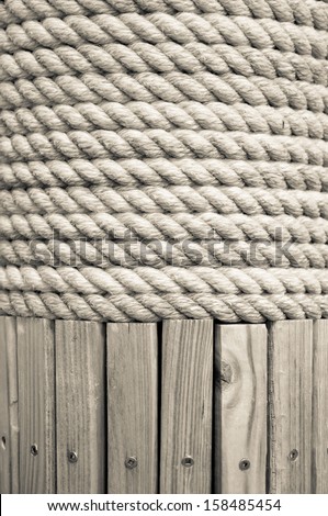 Braided white rope wrapped around a wooden post.  Wooden slats with metal screws are visible below the rope.  can be used as background or texture and has copy space