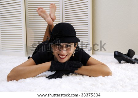 Beautiful woman in sequined black dress with black hat, gloves, laying on fluffy white rug