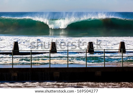 Ocean Wave Tidal Pool Large ocean wave swells crashing breaking front of tidal pool with sea waters washing into swimming pool