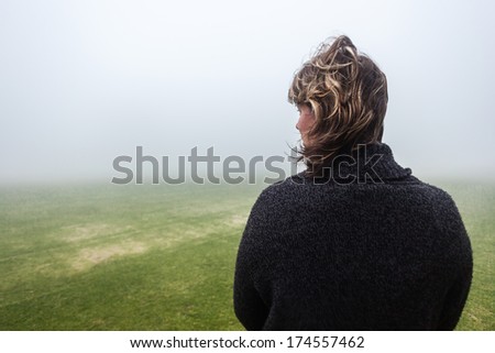 Woman Pondering Field Mist Woman unidentified standing pondering looks over green grass sports field covered in low cloud mist.