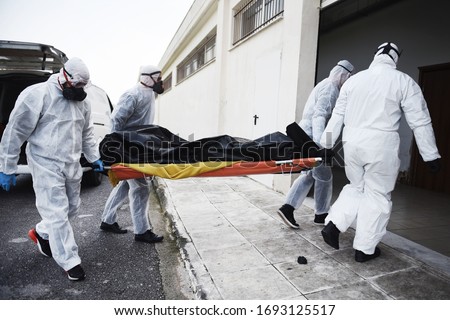 Funeral Home employees wear protective suits to protect themselves from Coronavirus, as they carry a dead body inside Bag. Foto stock © 